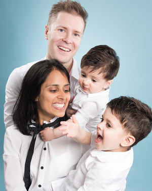 Family of four, two adults and two children, posing together against a light blue background.
