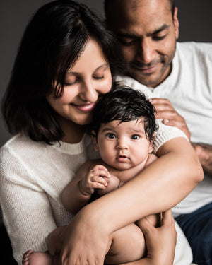 Family of three with a baby, mother holding the baby, father standing behind them.