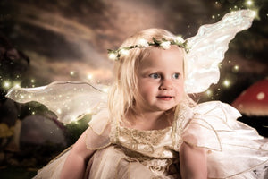Child dressed as an angel with fairy wings and a flower crown against a dark, starry sky.