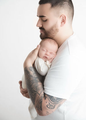 Dad with tattoos holding a newborn baby against a white background
