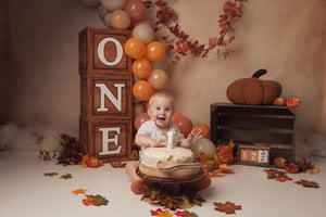 Baby celebrating a first birthday with a cake, balloons, and autumn-themed decorations.