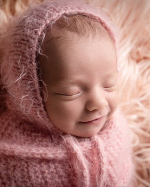 Newborn baby wrapped in pink fabric and bonnet on a soft pink surface