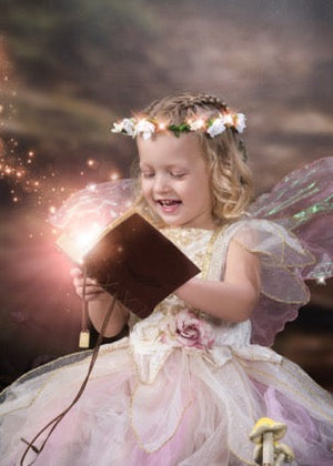 Young girl in fairy costume with wings holding a book in a fantasy setting reading magic book
