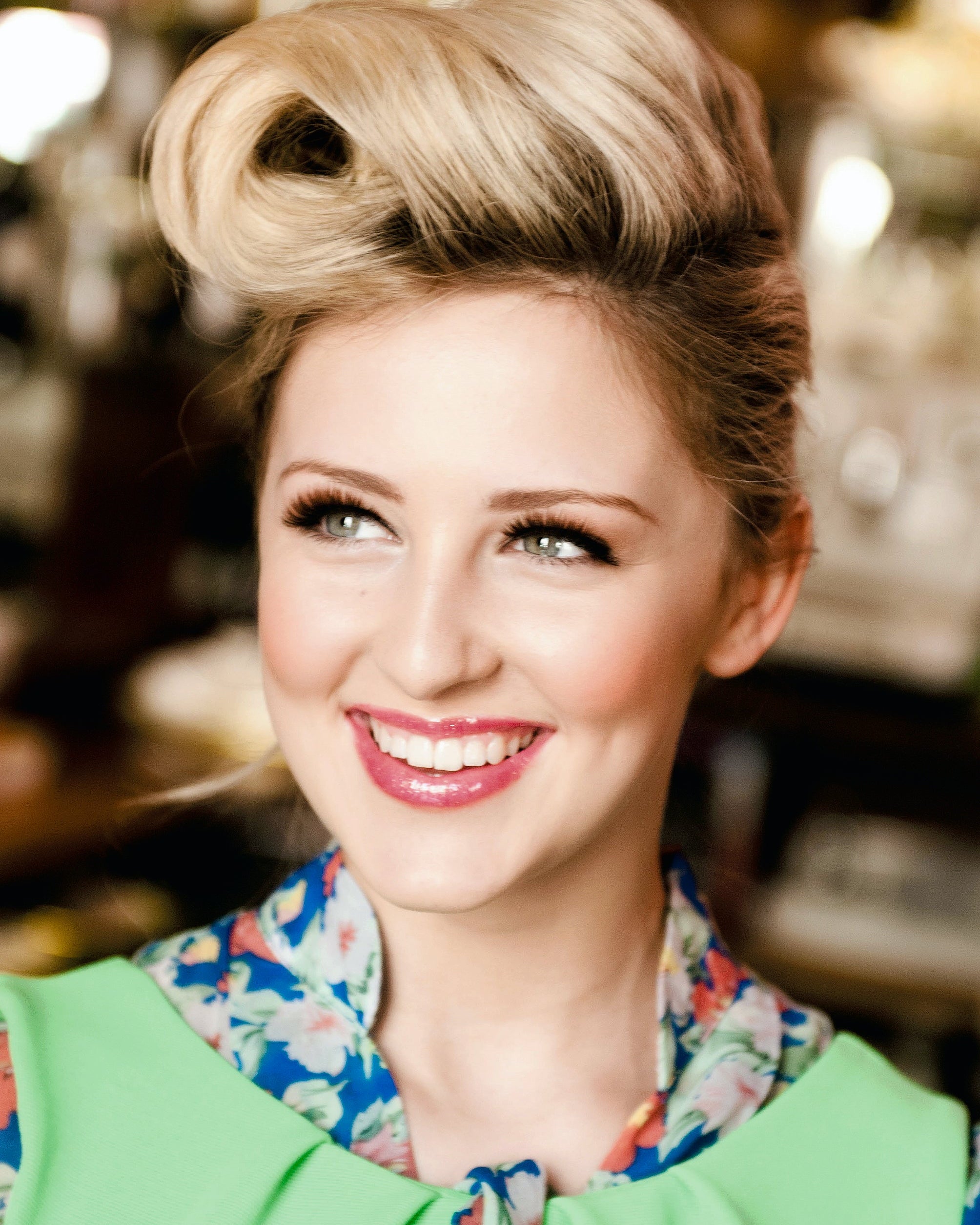 Woman with styled hair and a colourful outfit in a blurred indoor setting