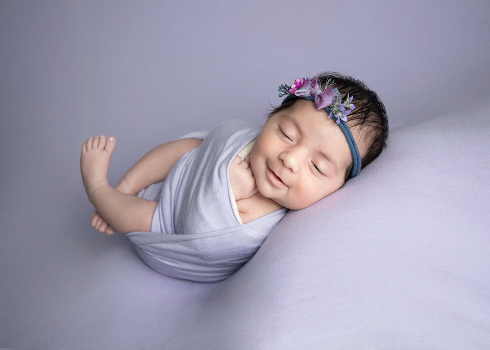 Newborn baby sleeping on a gray blanket with a floral headband