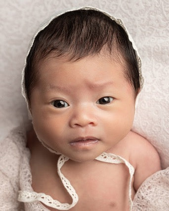 Newborn baby wearing a white bonnet on a soft, light-colored background