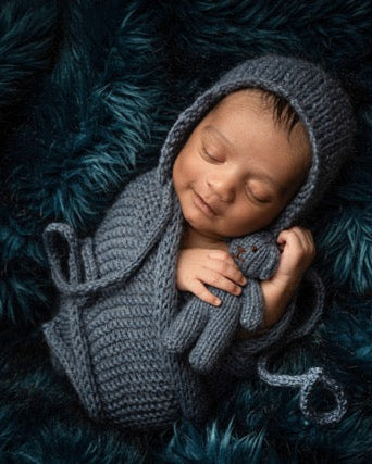Newborn baby wrapped in a gray crocheted blanket and hood on a dark blue textured surface