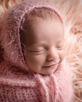 Newborn baby wrapped in pink fabric and bonnet on a soft pink surface